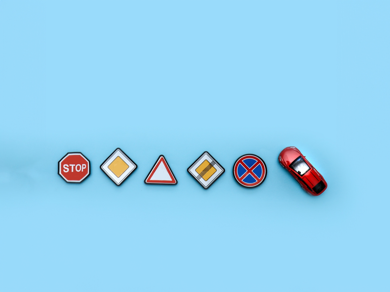 Road signs and toy car on blue background to show driving rules.