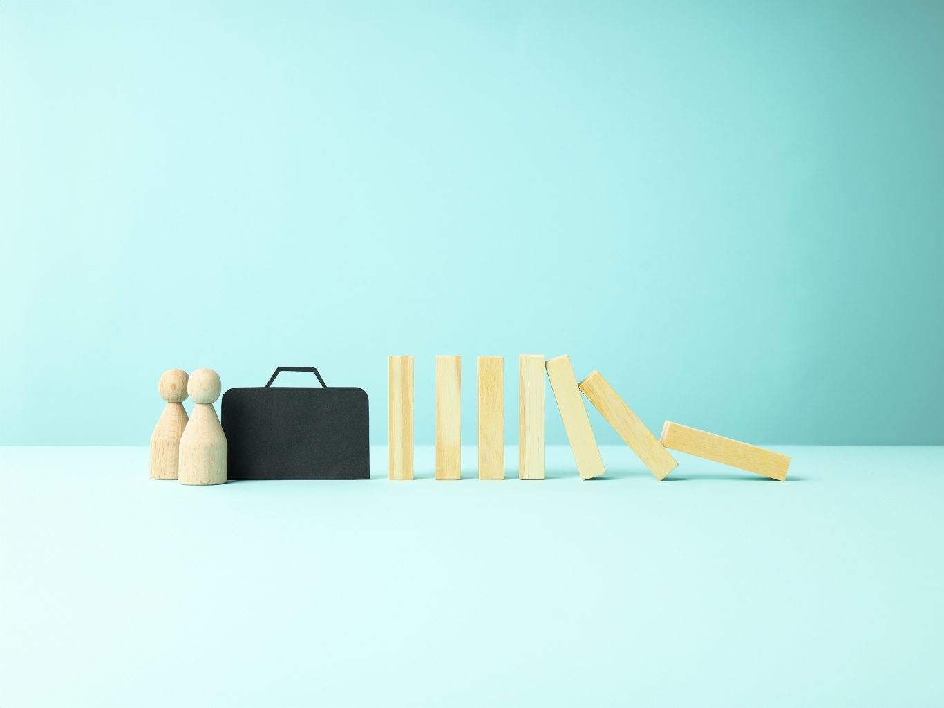Two wooden people with a briefcase with some wooden blocks tumbling over.