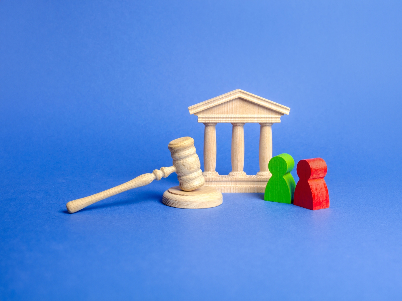 Two figures of people opponents stand near a wooden courthouse and the judges gavel to show settlement.